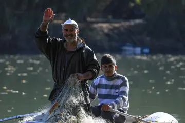 Dicle Nehri'nde küçük bir teknede balık ağıyla balıkçılık yapan baba ve oğlunun doğal nehir manzarası içindeki görüntüsü
