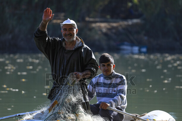 Dicle Nehri'nde küçük bir teknede balık ağıyla balıkçılık yapan baba ve oğlunun doğal nehir manzarası içindeki görüntüsü