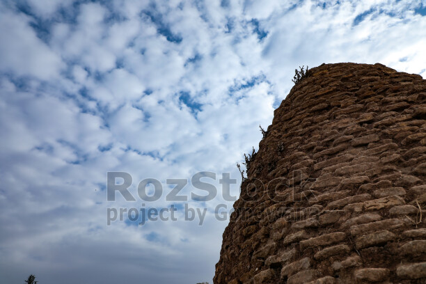 Şanlıurfa Harran Antik Kenti'ndeki tarihi taş duvarı ve etkileyici bulutlu gökyüzünü gösteren editoryal fotoğraf.
