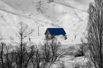 Karlı dağlar, mavi çatılı dağ evi ve kış manzarası