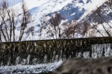 Karlı dağların önünde akan su, küçük şelale ve kış doğası