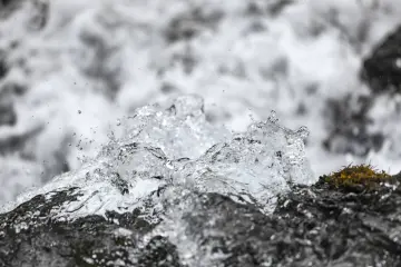 Karlı doğada kayalar arasında akan berrak su ve doğal kaynak