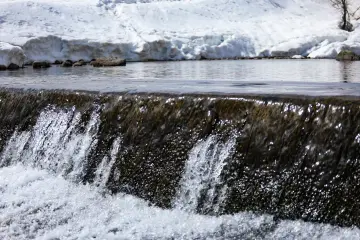 Karlı doğada akan dere, küçük şelale ve berrak su manzarası