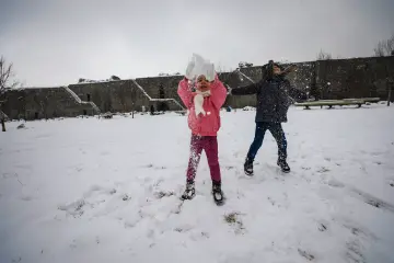 Yoğun kar yağışı altında tarihi bir kale avlusunda karla oynayan çocuklar görülüyor. Karla kaplı geniş alan, taş kale duvarları ve kış atmosferi, açık havada eğlence ve tarihi dokuyu bir arada yansıtıyor.
