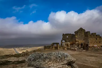 Zerzevan Kalesi kalıntıları ve bulutlu gökyüzüyle bütünleşen tarihi manzaranın panoramik görünümü.