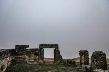 Zerzevan Kalesi taş kapısı ve tarihi kalıntılarının bulutlu gökyüzü eşliğinde etkileyici görünümü.