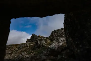 Zerzevan Kalesi taş açıklığından görülen kayalık arazi ve bulutlu gökyüzünün tarihi manzarası.